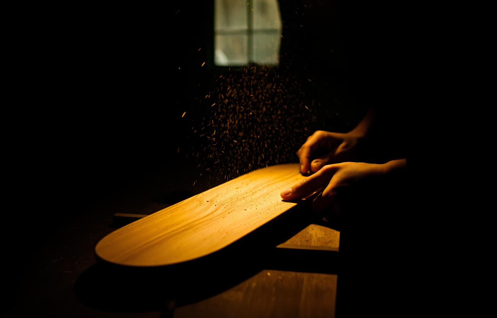 Hands shaping a fingerboard deck in the workshop